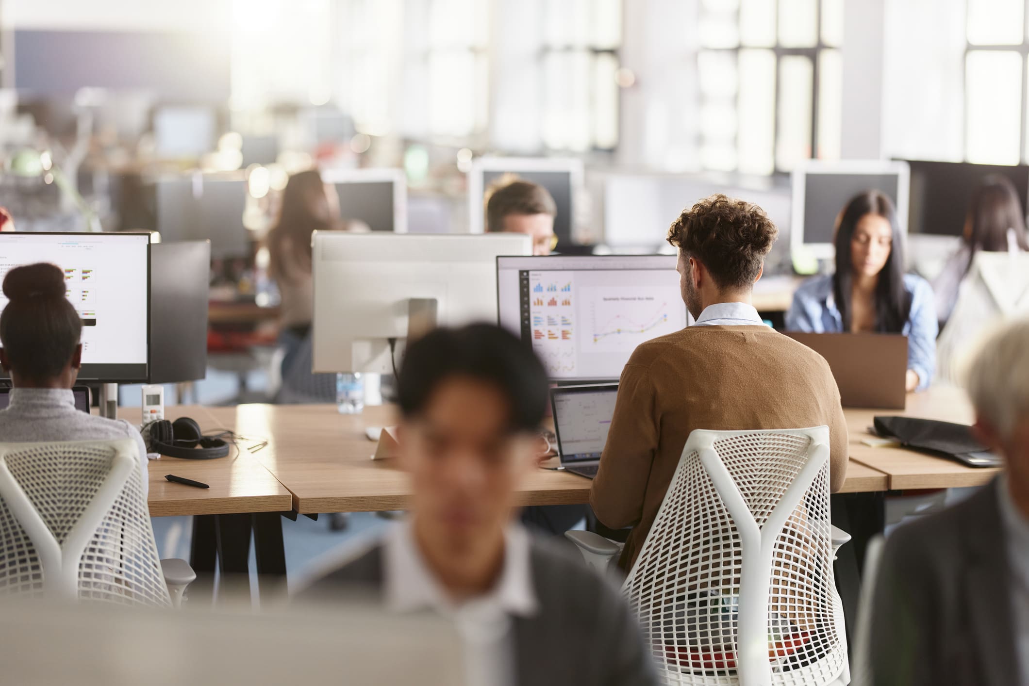 Back view of a male programmer working on computers among his colleagues in the office.